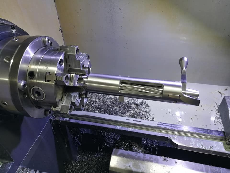 Metal lathe chuck holding a long cylindrical workpiece in a machine shop.