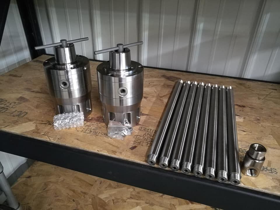 Metal machine parts and cylinders laid out on a workbench in a workshop setting