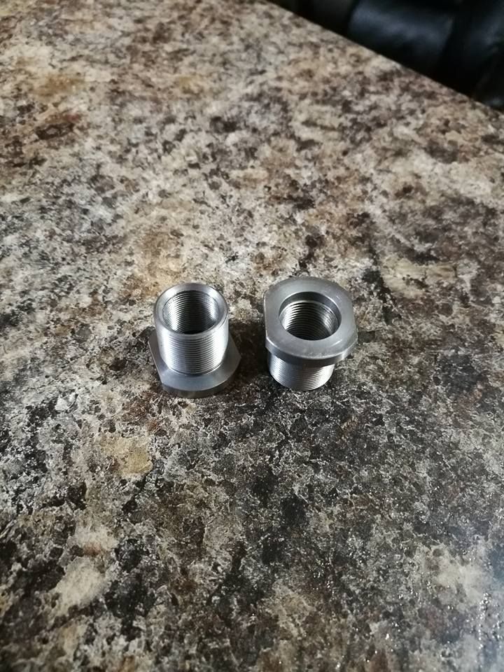 Two small silver metal threaded fittings on a speckled granite countertop.