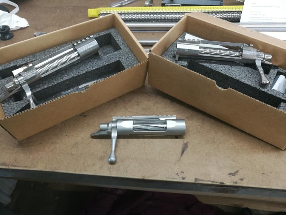 Two silver metal tools in cardboard boxes on a workbench, with one tool in the center foreground.