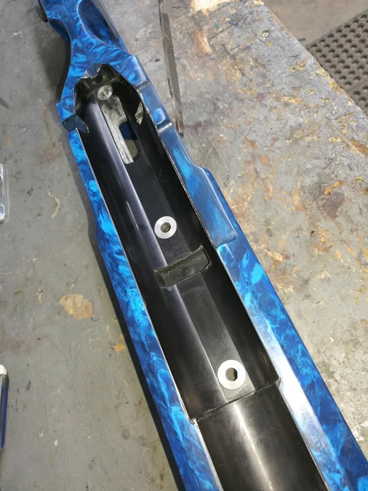 Blue and black plastic car part with mounting holes, lying on a worn concrete floor