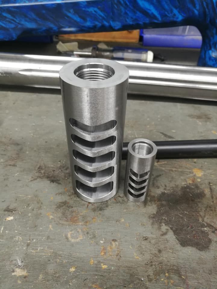 Two silver metal threaded parts standing on a workshop floor, one large and one small