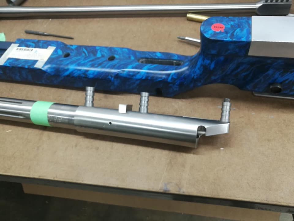 Blue rifle stock and silver barrel components laid on a workbench with a brush above.