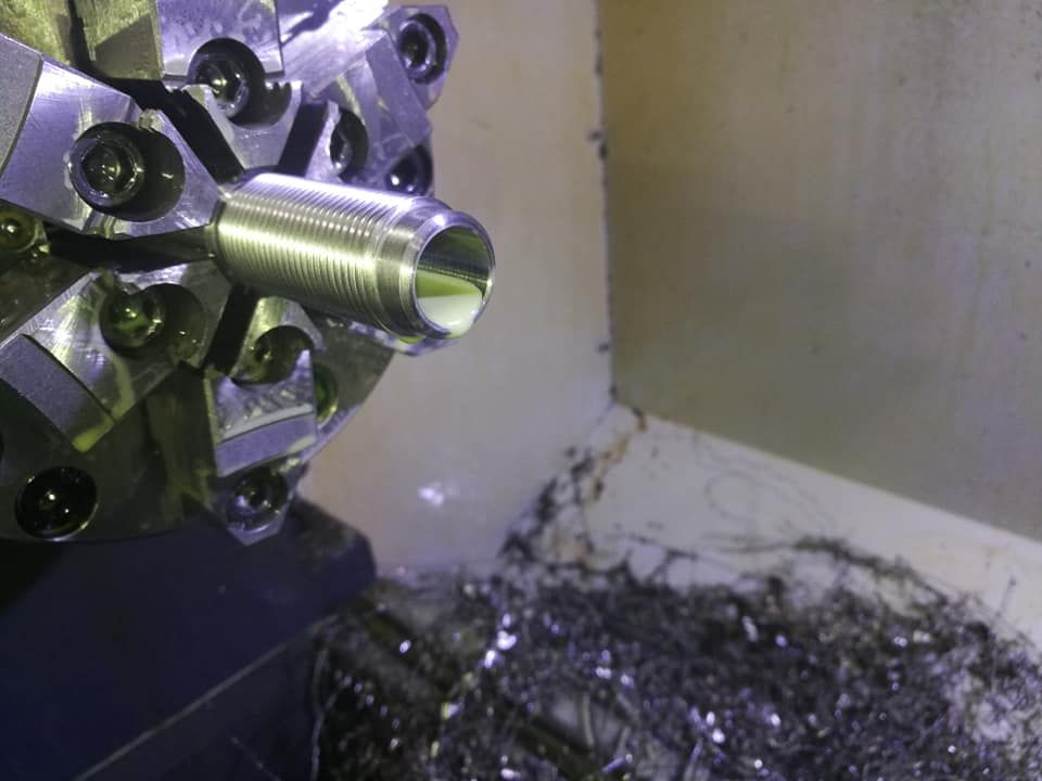 Metal lathe cutting a threaded bolt, with curled shavings on the machine bed