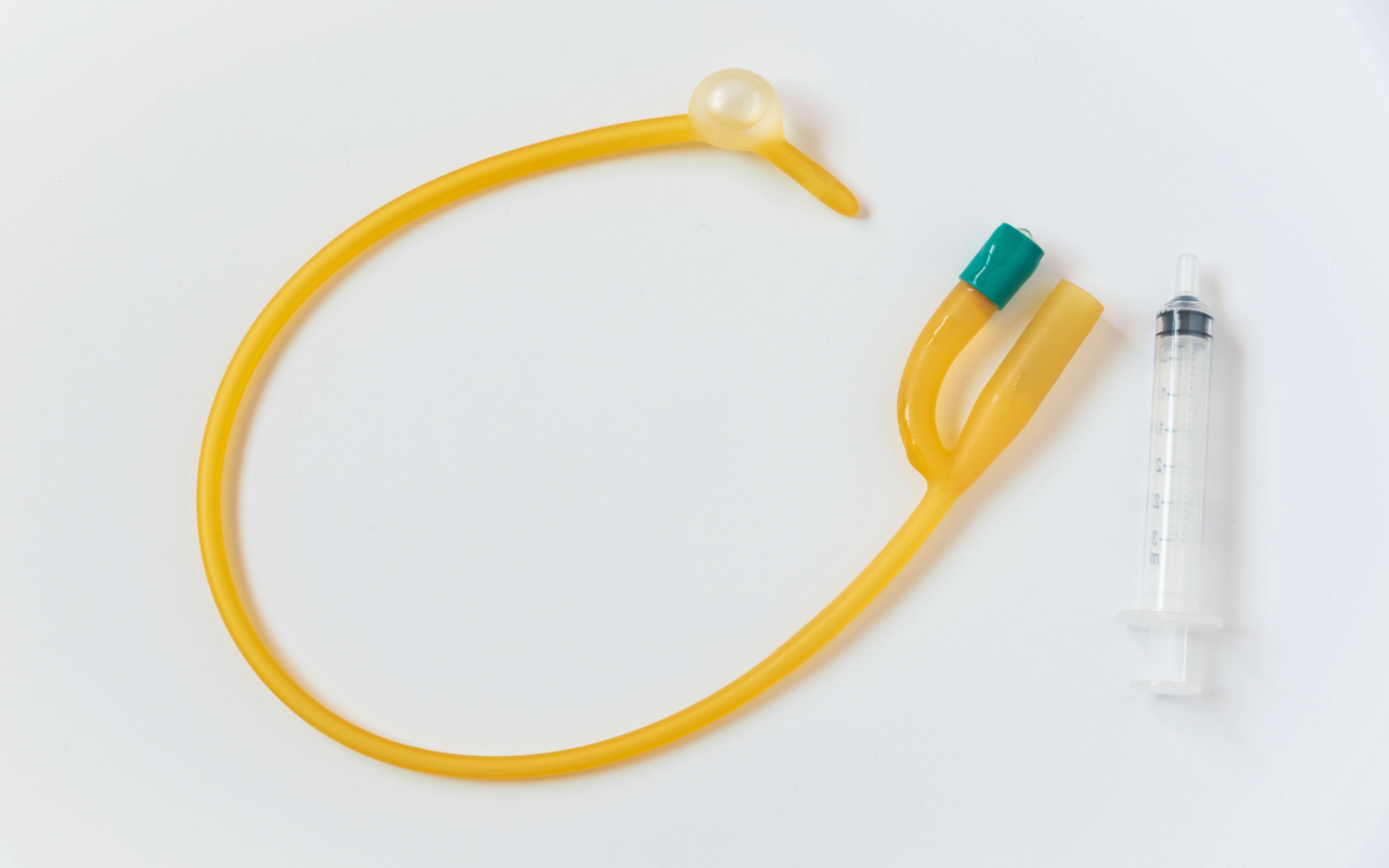 Yellow Suprapubic Catheter with green connectors and a small syringe on a white background
