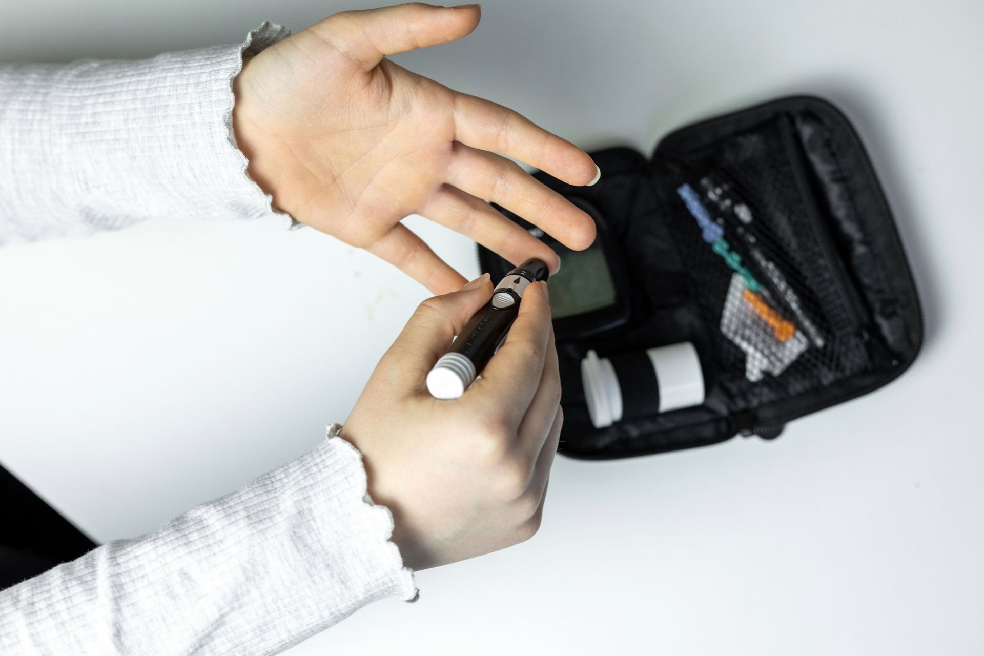 Person using a finger prick device to check blood glucose, open kit in the background.