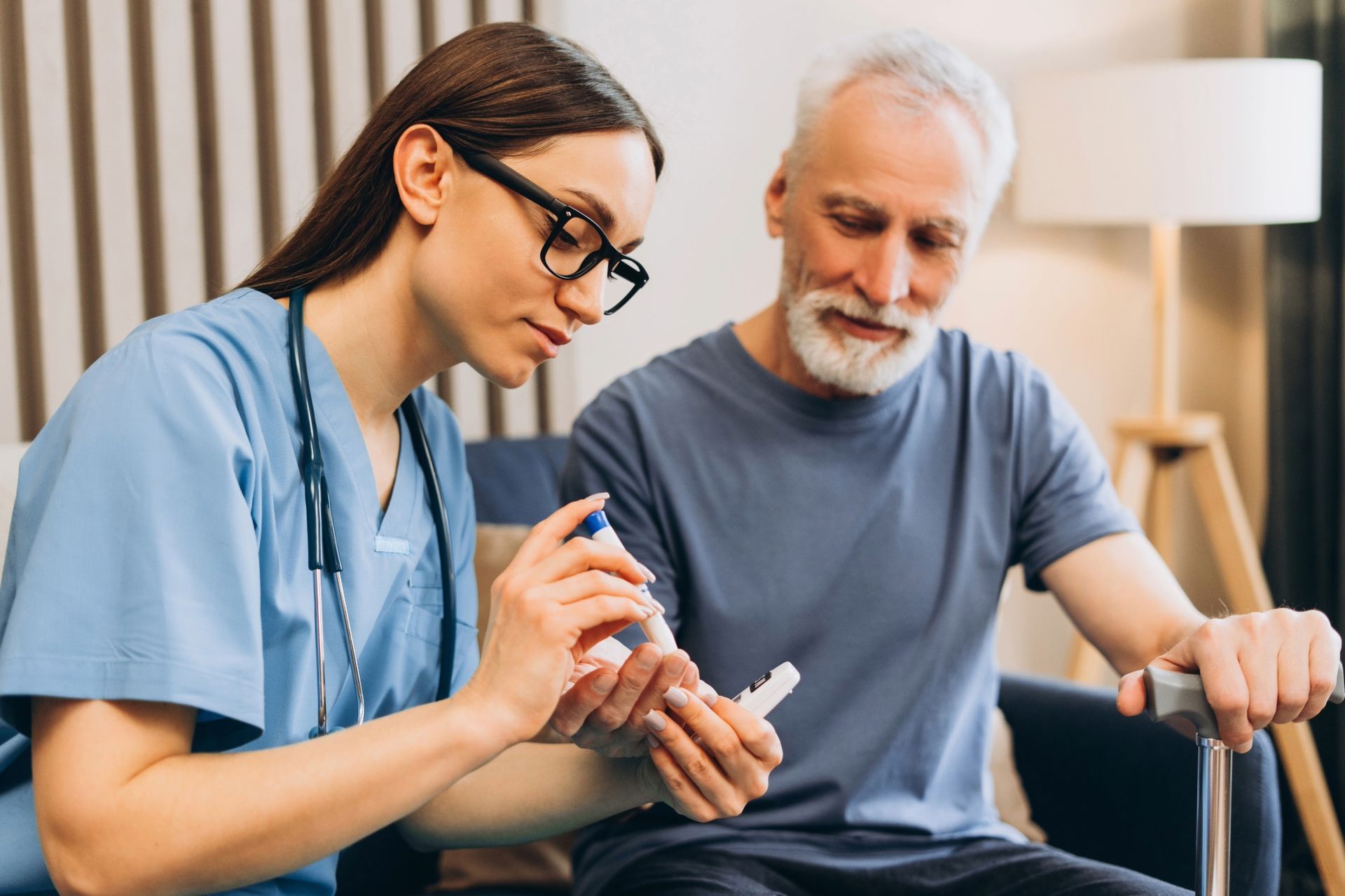 Nurse applying ointment to a man's hand; he holds a cane, and they are indoors.