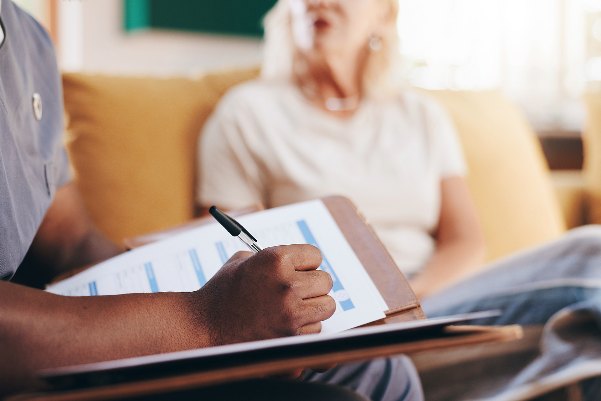 Continence Nurse Consultant (CNC) writing clinical notes during an NDIS continence assessment with a