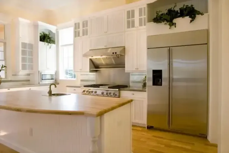 Bright kitchen with white counters, black island, and dining table by a window overlooking greenery.
