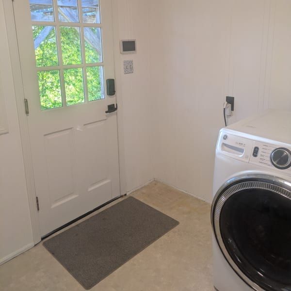 Laundry room with white door, gray mat, and a front-loading washer beside the wall