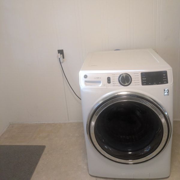 White front-loading washer and dryer in a sparse laundry room beside a wall outlet