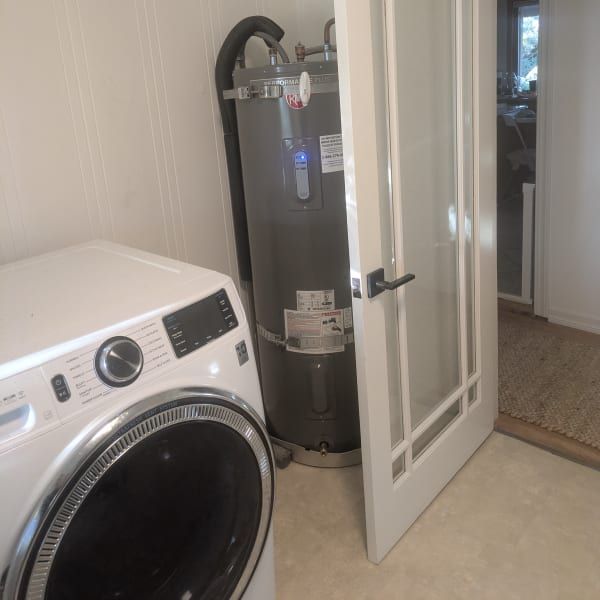 Laundry room with a front-load washer, water heater, and open white door to a hallway