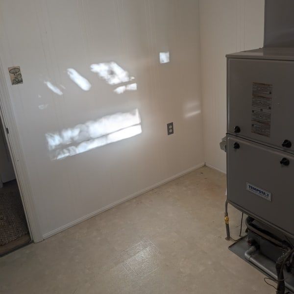 Empty utility room with beige walls, sunlit shadows, and a large HVAC unit on the right.