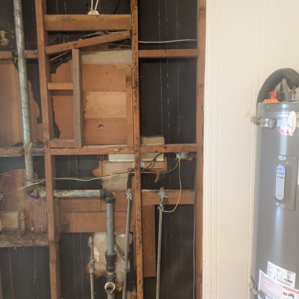 Exposed wall studs with plumbing and wiring beside a water heater in a utility area