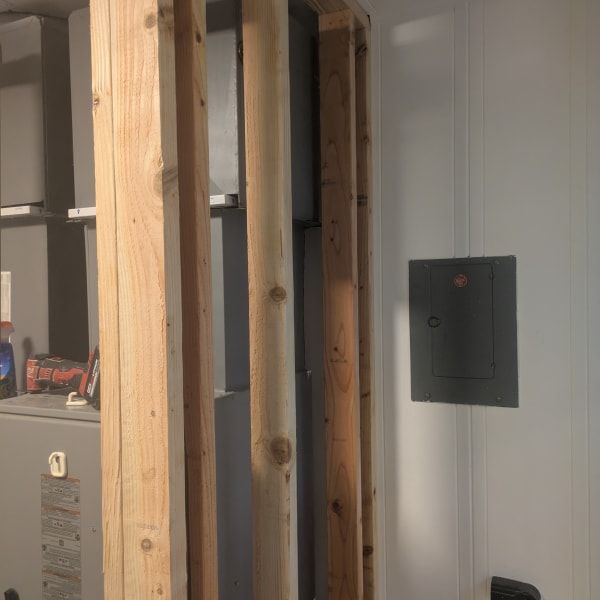Exposed wooden framing in an unfinished room with a gray wall panel and electrical box.