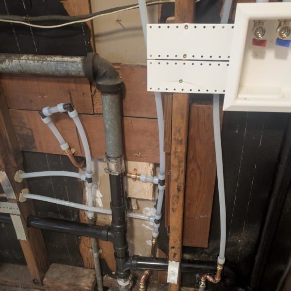 Exposed plumbing and pipes inside a wall, with valves and utility boxes in a basement or utility room