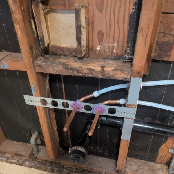 Open wall framing with plumbing pipes, copper fittings, and a gray metal support bracket.