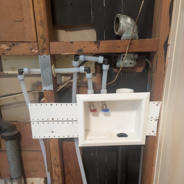 Bathroom plumbing under renovation with exposed pipes and a white sink cabinet.
