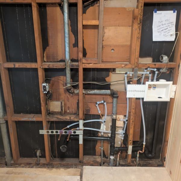 Exposed wall framing with plumbing, wiring, and a utility panel in a partially unfinished room