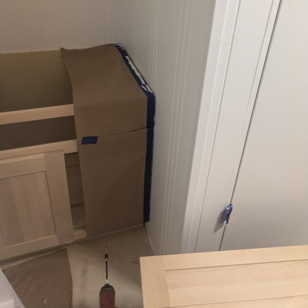 Cardboard boxes stacked beside a white door in a narrow hallway, with a drill on the floor.