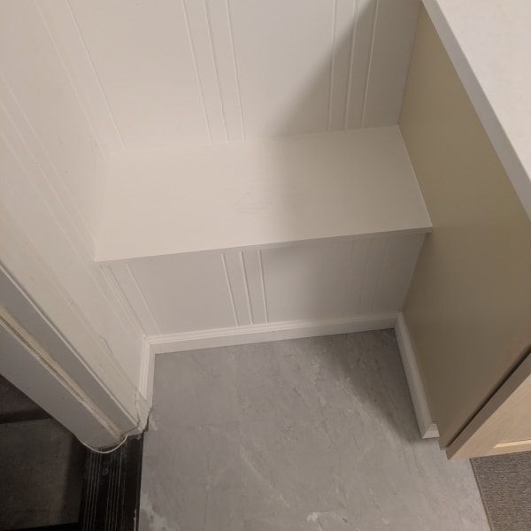 Empty corner with white built-in shelves, light walls, and a gray floor near a doorway.