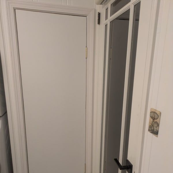 White interior door ajar in a hallway, with a black handle and beige wall switch on the right
