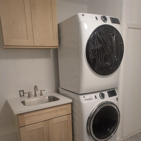 Laundry room with stacked washer and dryer beside a small sink and wooden cabinet.