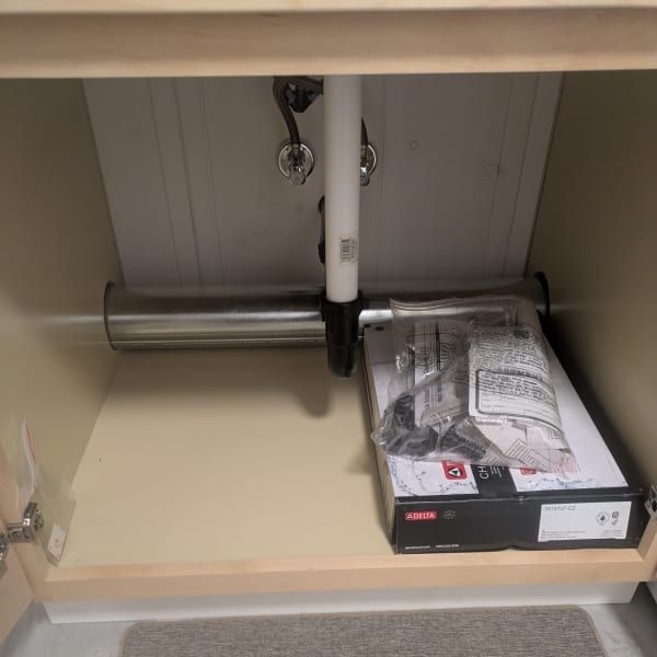 Empty cabinet with a shelf, pipe, and a package of hardware or parts on the right.