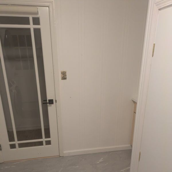 Small empty room with white paneled walls, a glass door on the left, and a white door on the right.
