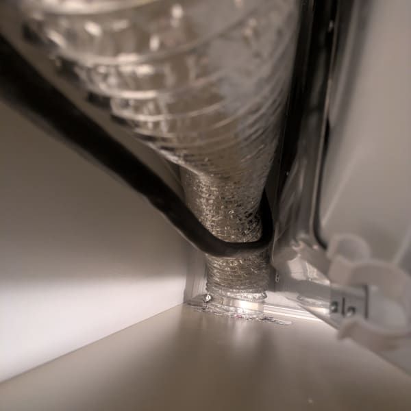 Close-up of a vented duct or hose inside a white appliance, with black trim and textured plastic surface.