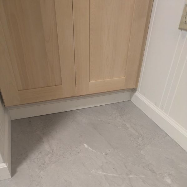 Gray tile floor beside light wood cabinets and white paneled walls in a corner
