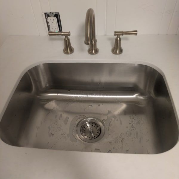 Stainless steel kitchen sink with faucet and two handles beneath a white tile backsplash.