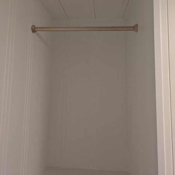 Empty closet with a single wooden hanging rod on white walls