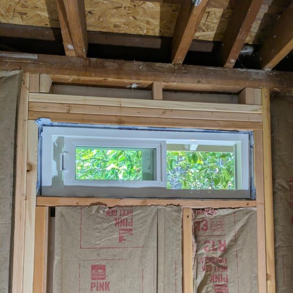 Unfinished wall with a small horizontal window and exposed insulation under roof framing