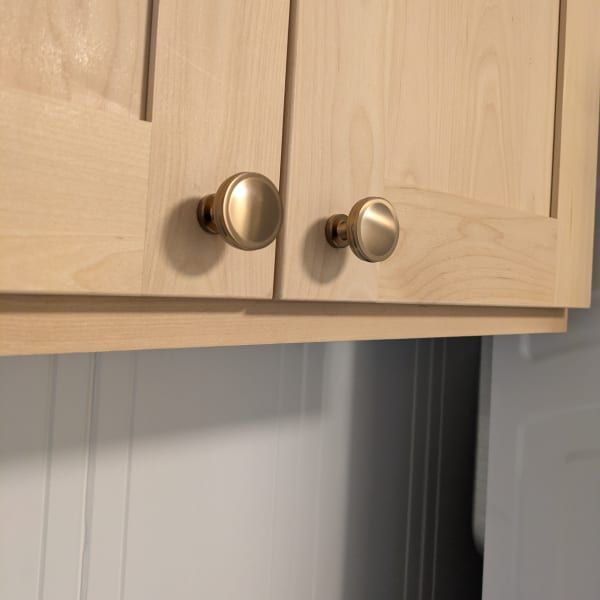 Light wood kitchen cabinets with two round metal knobs above a gray wall.