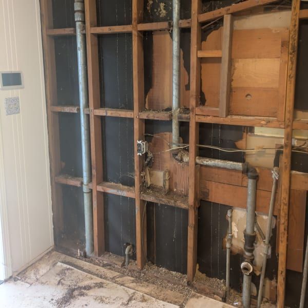 Exposed wall framing with plumbing pipes and torn drywall during interior renovation