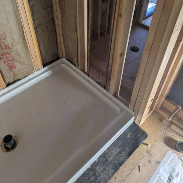Partially installed shower base in a framed bathroom under construction