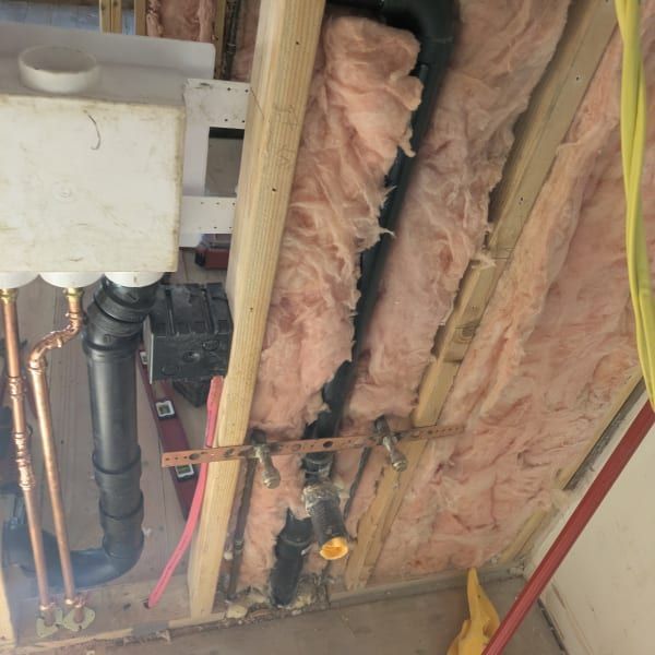 Exposed plumbing and pink insulation in an unfinished wall cavity during home construction.