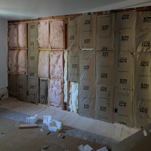 Insulated room under construction with pink foam and gray vapor barrier on the walls.