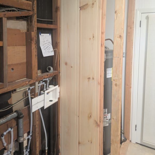 Open wall with exposed plumbing and wiring beside a pine door panel in a utility area