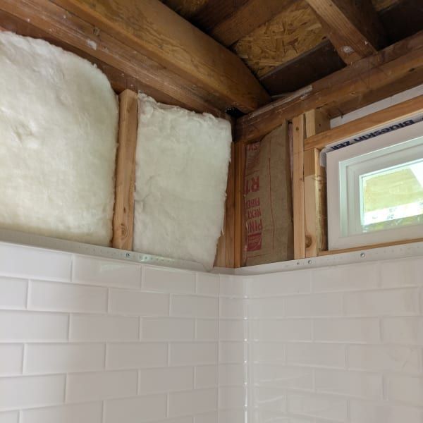 Partially renovated bathroom with exposed wall insulation above white tile and a small window