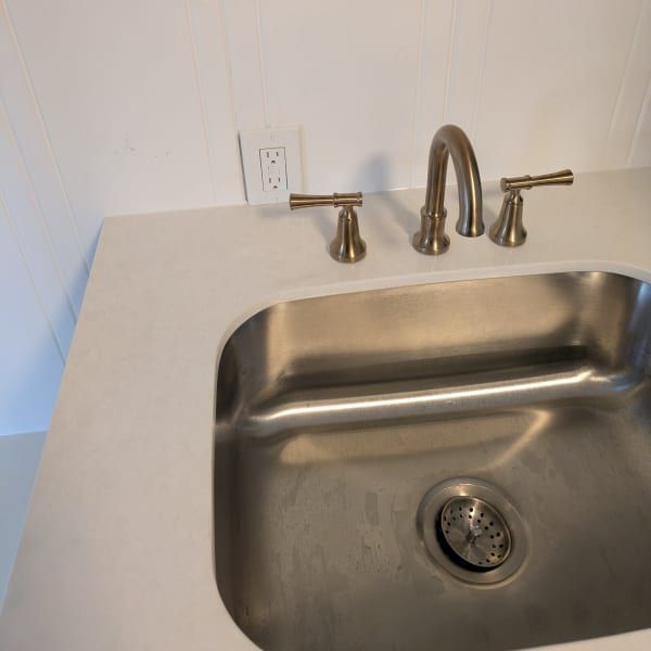 Stainless steel kitchen sink with chrome faucet and white countertop against a light wall.