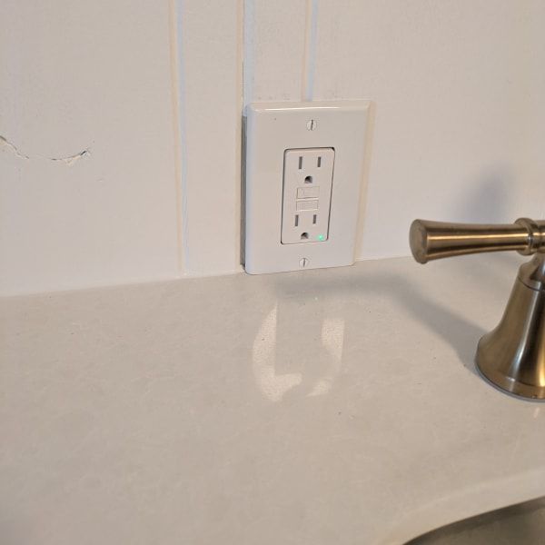 Bathroom sink with white wall outlet above a beige countertop and metal faucet handle