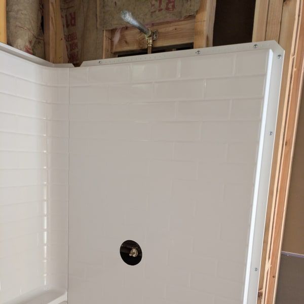 White tiled shower stall under construction with a drain opening and exposed framing above