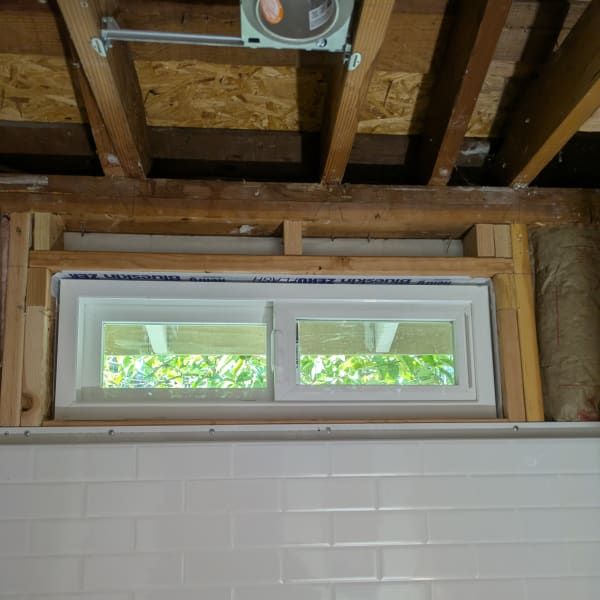 New white-framed window set into exposed wooden wall framing above white tile.
