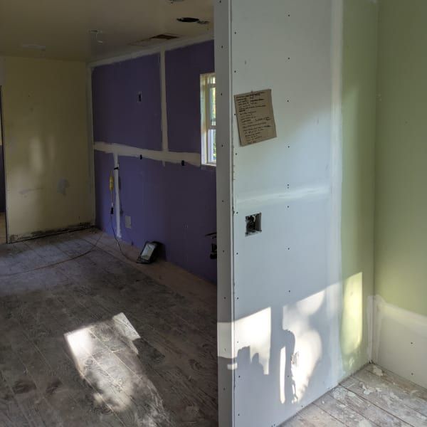 Partially renovated room with purple wall, white drywall, and sunlight on the floor