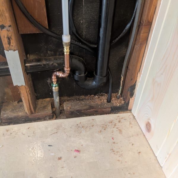 Exposed copper pipes and wall framing behind a drywall opening near a floor edge
