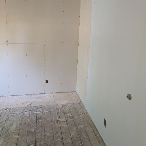 Empty room under renovation with unfinished drywall and bare wooden floorboards.