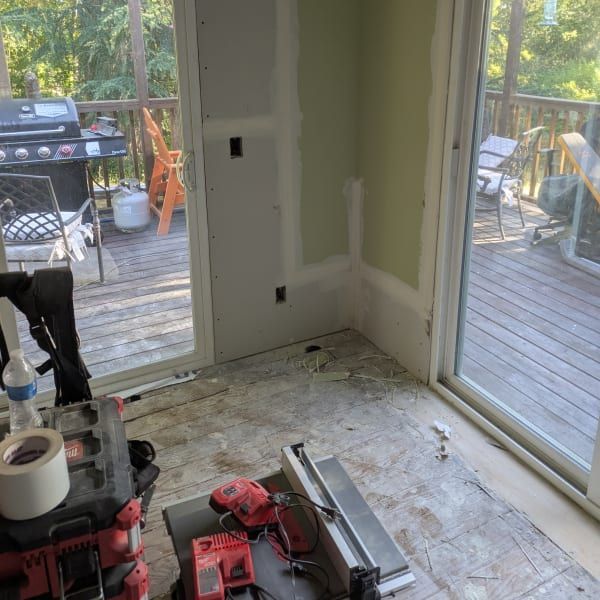 Partially renovated room with drywall patches, tools on the floor, and deck doors to a wooden patio