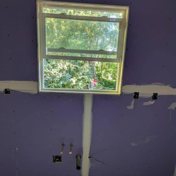 Purple interior wall with a centered window and exposed wiring under renovation.